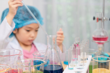 Asian little girl playing with fun as a scientist working in a lab equipped with colored glass tubes. Focus is tube.