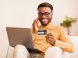 Man talking on cellphone using credit card and laptop indoor