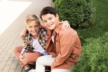 two cheerful brothers smiling while sitting on pavement and looking at camera