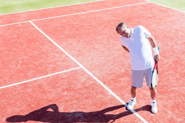 Full length of senior man standing with backache on red court during match on sunny day