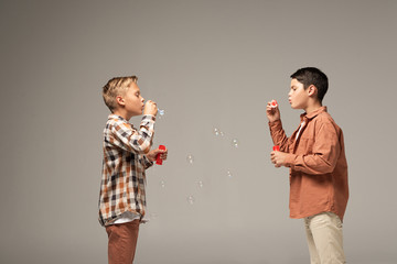 side view of two brothers blowing soap bubbles isolated on grey