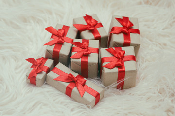 Set of gift boxes wrapped in craft paper and tie red satin ribbon. White fur background. Christmas presents. Holiday mood. New year decor. Gift exchange.
