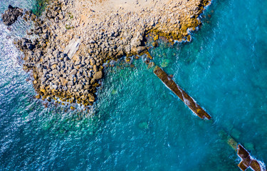Aerial top view of sea waves hitting rocks on beach with turquoise sea water. Amazing rock cliff seascape in Greece coastline. Drone shot.