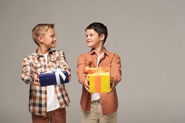 two brothers smiling at each other while holding blue and yellow gift boxes isolated on grey