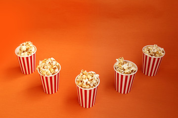 five striped red, white paper cups with popcorn on a bright orange background, close-up, copy space, fast food concept
