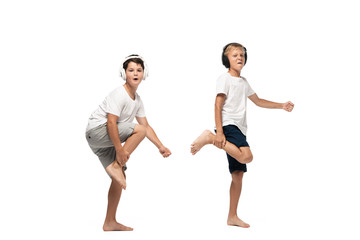two cheerful brothers looking at camera and dancing in headphones on white background