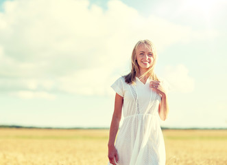 Fototapeta na wymiar happiness, nature, summer, vacation and people concept - happy smiling young woman or teenage girl on cereal field
