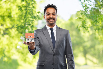 real estate business and people concept - indian man realtor with house model over green natural...