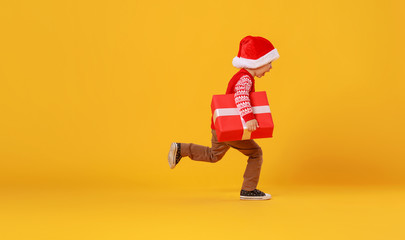 happy funny child boy in red  running with Christmas gift on yellow background.