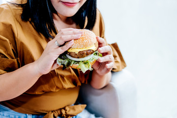 Obese women are happy With eating hamburgers, which consist of meat, fresh vegetables, breads and cheese with white background, to food and healthy concept.