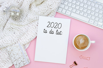 Woman's workspace with knitted sweater, keyboard and coffe cup on a pink background flat lay. 2020...