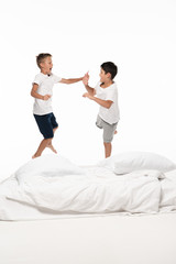 two excited brothers levitating over bed and looking at each other isolated on white