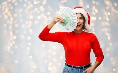 christmas, holidays and finance concept - happy smiling young woman in santa helper hat holding...