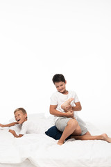 cheerful boy jokingly breaking leg of screaming brother while having fun on bed isolated on white