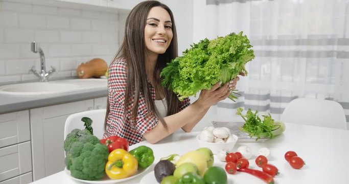 Beautiful young woman smelling fresh salad in kitchen and looking to camera, healthy lifestyle, vegetarian diet