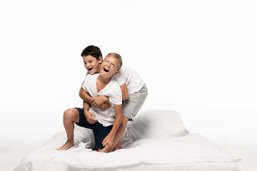 cheerful boys imitating fighting while having fun on bed isolated on white