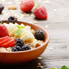 Fruit healthy muesli with banana strawberry almonds and blackberry in clay dish on wooden kitchen table