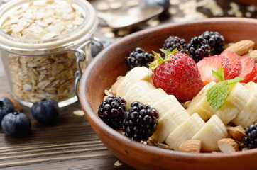 Fruit healthy muesli with banana strawberry almonds and blackberry in clay dish on wooden kitchen table