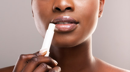 Black woman applying lip balm over grey background, closeup - obrazy, fototapety, plakaty