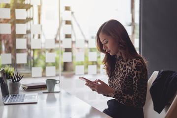 Attractive young asian businesswoman sitting using app on smartphone at office.