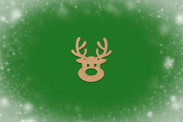 Wooden Christmas toy Deer head on a green isolated background with the effect of falling snow. Merry Christmas and Happy New Year concept. Minimalistic style. Flat lay, top view