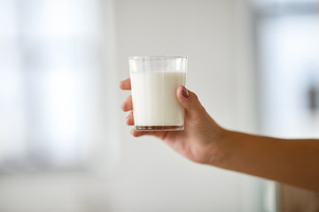 food, eating and dairy products concept - close up of female hand holding glass of milk