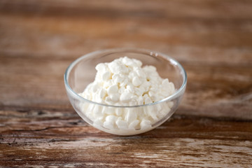Fototapeta na wymiar food and dairy products concept - close up of homemade cottage cheese in glass bowl on wooden table