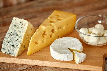 food and eating concept - different kinds of cheese on wooden cutting board