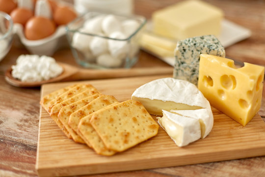 Food And Eating Concept - Close Up Of Salty Crackers And Cheese On Wooden Board