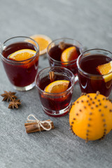 christmas and seasonal drinks concept - glasses of hot mulled wine with orange and cinnamon on grey background