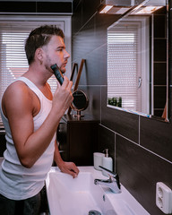 Close up portrait of a serious man shaving beard with an electric razor, Handsome young bearded man...