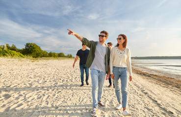 friendship, leisure and people concept - group of happy friends walking along beach in summer