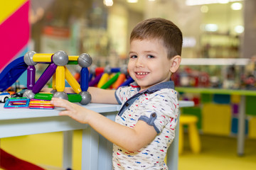 Happy funny little boy child playing with lots of toy cars indoor. Kid boy wearing colorful shirt and having fun at nursery