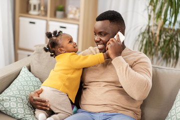family, fatherhood and technology concept - happy african american father with baby at home calling on smartphone