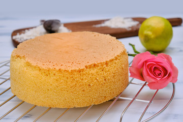 Fresh baked cake biscuit on a metal rack, side view. White background with pastry, flower, lemon and flour.