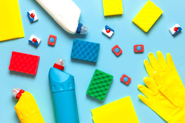 House cleaning concept. Household chemicals, disinfectant, bleach, antibacterial gel, yellow rubber gloves, sponge, rags, dishwasher tablets on blue background. Flat lay top view. Cleaning accessories