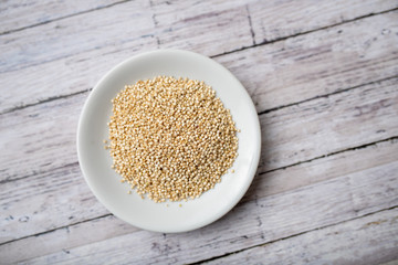 Raw white quinoa seeds on white wood background in a small plate