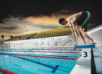 Swimmer jumping from starting block in a swimming pool