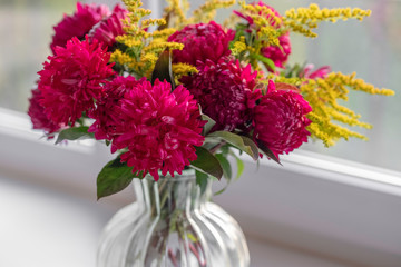 Bouquet of magenta dahlias. Fresh bunch purple pink with yellow peonies roses flower in glass vase on the window sill, white background. Autumn time concept. Still life, rustic style.