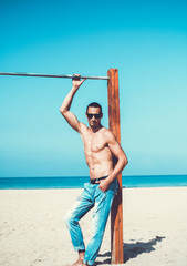young muscular man resting and posing on the beach. Wearing sunglasses