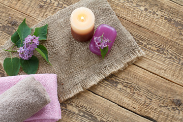 Fototapeta na wymiar Towels, soap, candle and lilac flowers on wooden background.