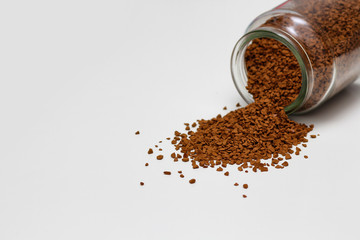 Open glass jar with instant coffee spilled out. White solid background.
