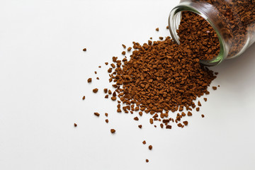 Open glass jar with instant coffee spilled out. White solid background.
