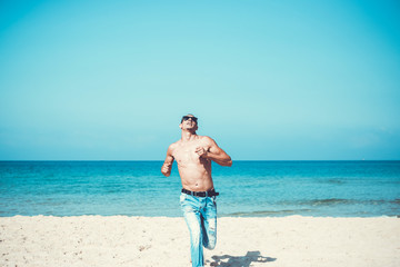 Obraz na płótnie Canvas young muscular man resting and posing on the beach. Run towards us
