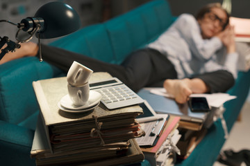 Stressed businesswoman sleeping on a couch with lots of paperwork