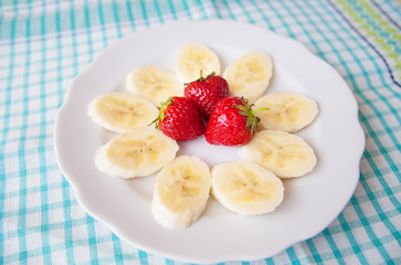 banana and strawberries on white plate and a colorful napkin