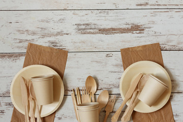 Eco friendly disposable dishes made of bamboo wood and paper on white wooden background.
