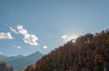 Obraz premium Profile of a mountain slope stripped by a forest. Peaked peak in a bluish haze. Clouds on a blue sky. The setting sun is breaking through the rays of the trees at the top with its rays.