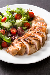 Grilled chicken breast with vegetables on a plate on black background