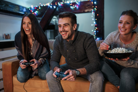 Group of best friends sitting at home on pleasant evening and playing games on console.They challenge each other to win .	